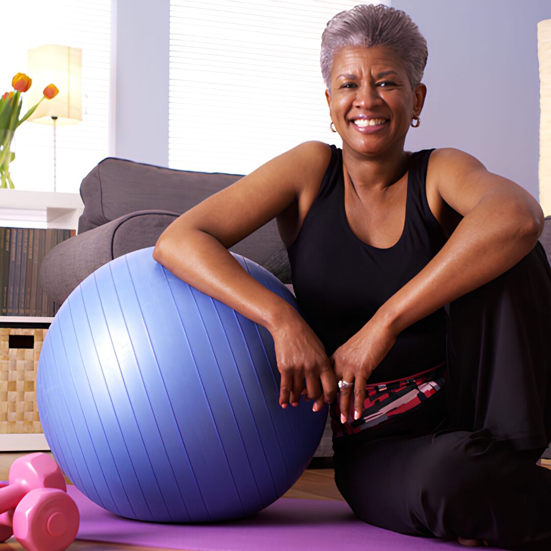 A woman sitting on the floor next to an exercise ball.