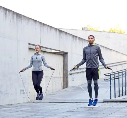 Two people jumping rope on a sidewalk near some stairs.