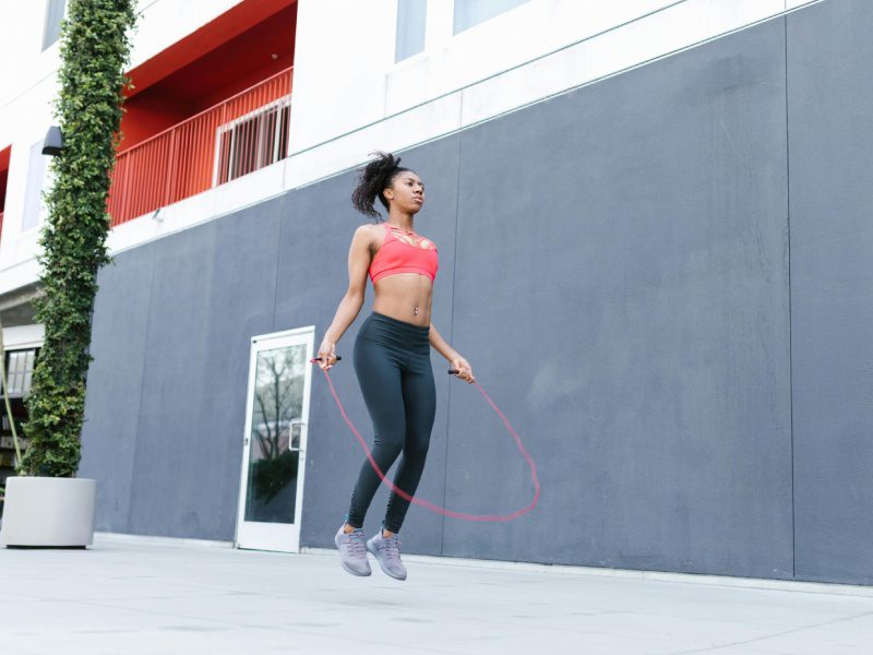 A woman jumping rope on the sidewalk in front of a building.